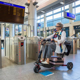 A lady travelling at a station with her ATTO sport mobility scooter and a suitcase under the chair